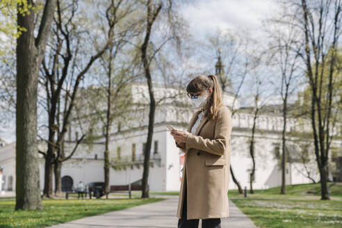 Woman wearing FFP2 mask and using smartphone in a park - AHSF02510