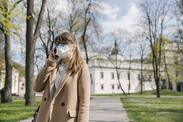 Frau trägt FFP2-Maske und benutzt Smartphone in einem Park - AHSF02511