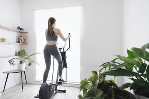 Frau beim Training auf dem Ellipsentrainer zu Hause - AHSF02524