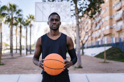 Junger Mann hält Basketball auf Basketballplatz - EGAF00009