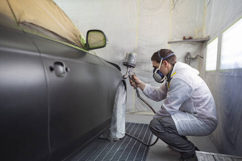 Karosserielackierer lackiert Auto in Lackierkabine, lizenzfreies Stockfoto