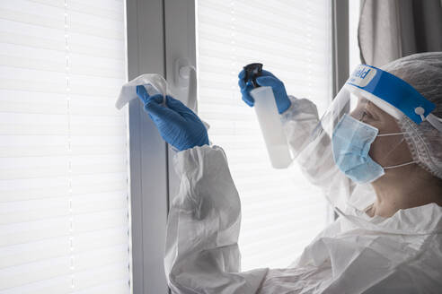 Frau in Schutzkleidung desinfiziert Tuch am Fenster - SNF00042