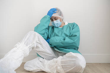 Exhausted woman wearing personal protective equipment sitting on the floor - SNF00048