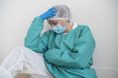 Exhausted woman wearing personal protective equipment sitting on the floor - SNF00049