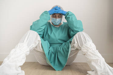 Exhausted woman wearing personal protective equipment sitting on the floor - SNF00051