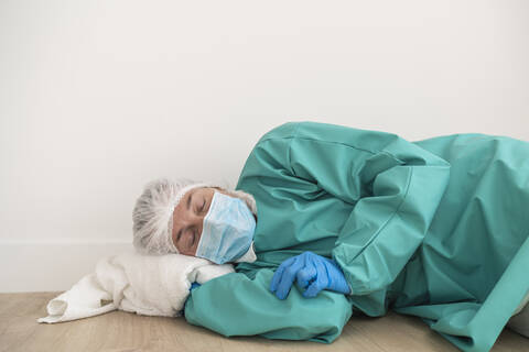 Exhausted woman wearing personal protective equipment lying on the floor stock photo