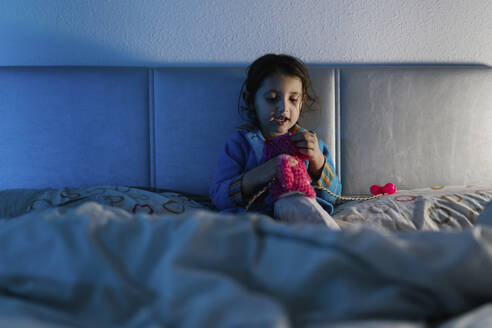 Portrait of little girl sitting on bed playing with her toy - EGAF00043