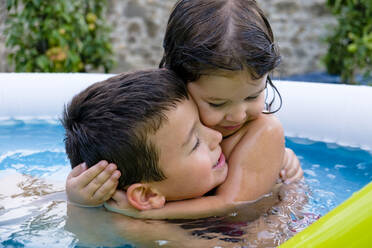 Bruder und seine kleine Schwester umarmen sich im Schwimmbad - MGIF00928