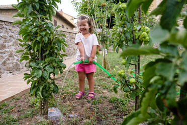 Laughing little girl watering tree in the garden - MGIF00930