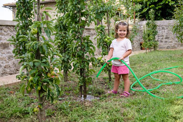 Lächelndes kleines Mädchen bewässert Baum im Garten - MGIF00931