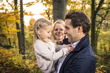 Smiling woman looking at daughter playing with father in forest - WFF00401