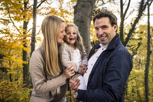 Lächelnder Mann, der seine Tochter trägt, während er neben einer schwangeren Frau im Wald steht - WFF00403