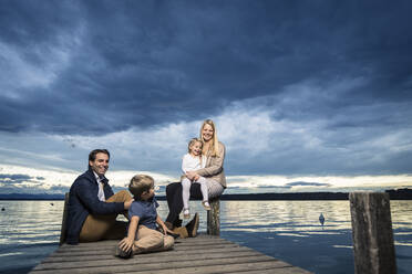 Full length of happy family sitting on jetty at Starnberger See against cloudy sky - WFF00407
