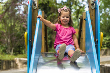 Smiling girl sliding on slide with friends at park stock photo