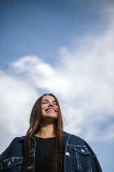 Niedriger Blickwinkel auf eine glückliche junge Frau, die vor dem Himmel steht - GRCF00191