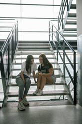 Full length of young female students sharing smart phone while sitting on steps at university - GRCF00193