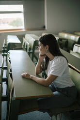 Seitenansicht einer nachdenklichen jungen Frau, die am Schreibtisch sitzt und wegschaut - GRCF00197