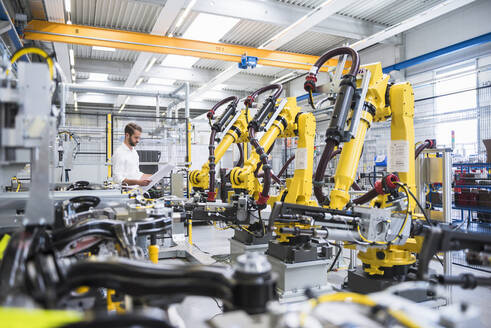 Junger Ingenieur liest Papier, während er neben Roboterarmen in der automatisierten Industrie steht - DIGF10402