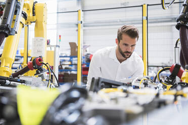 Confident young male engineer examining automated machinery in robotic factory - DIGF10407