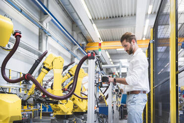 Side view of confident robotics expert examining machinery in factory - DIGF10408