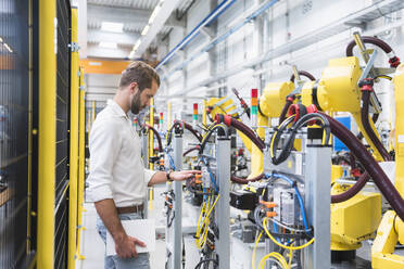 Junger männlicher Ingenieur betrachtet den Roboterarm einer Maschine in einer automatisierten Fabrik - DIGF10410