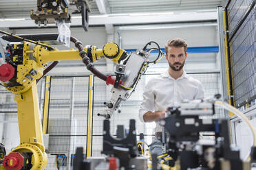 Confident male robotics expert looking at machinery in automated industry - DIGF10416
