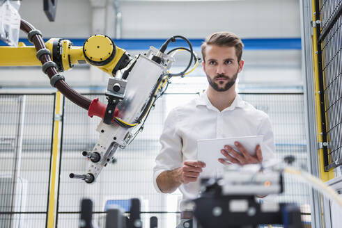 Junger Robotik-Ingenieur schaut weg, während er an einer Maschine in einer Fabrik steht - DIGF10417