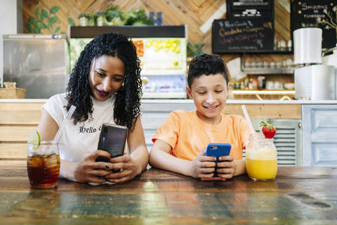 Lächelnde Mutter und Sohn benutzen Smartphones, während sie im Restaurant sitzen, lizenzfreies Stockfoto