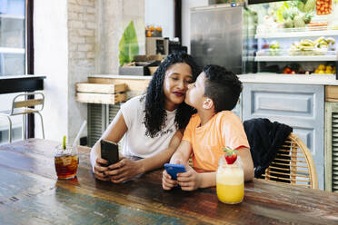 Junge küsst Mutter, während er mit Handy und Getränken im Restaurant sitzt - DGOF00962
