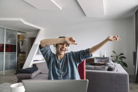 Glückliche Frau mit Kopfhörern und Laptop zu Hause, lizenzfreies Stockfoto
