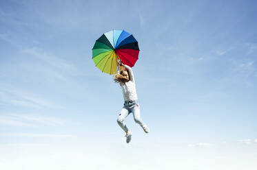 Niedrigen Winkel Ansicht von Mädchen springen mit bunten Regenschirm gegen blauen Himmel - JCMF00700