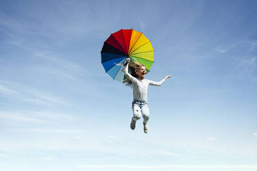 In voller Länge von unbeschwerten Mädchen springen mit bunten Regenschirm gegen blauen Himmel - JCMF00701