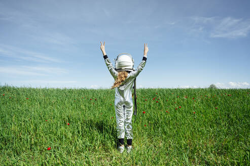 Rear view of girl in astronaut costume standing with peace sign on grass - JCMF00704