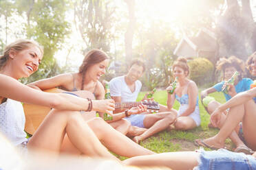 Junge Freunde hängen ab, spielen Gitarre und trinken Bier im sonnigen Sommergras - CAIF27192