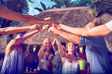 Junge Freunde stoßen mit Alkohol in Schnapsgläsern auf einer Party am Pool an - CAIF27201