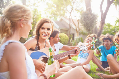 Junge Freundinnen hängen ab, spielen Gitarre und trinken Bier im Sommergras - CAIF27203