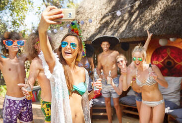 Enthusiastic young friends drinking and taking selfie at sunny summer poolside party - CAIF27206