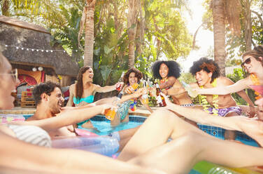 Enthusiastische Freunde trinken, stoßen mit Bierflaschen und Cocktails auf einer Sommerparty am Pool an - CAIF27209