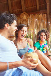Lachende junge Freunde, die am Sommerpool einen Kokosnusscocktail trinken - CAIF27219