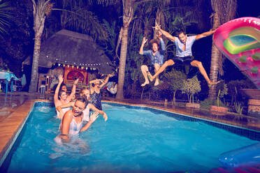 Exuberant young men friends jumping into swimming pool at night - CAIF27220