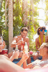 Junge Freunde hängen zusammen ab und stoßen mit Bierflaschen im sonnigen Sommerschwimmbad an - CAIF27226