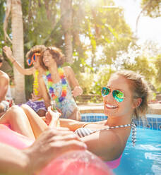 Portrait smiling, confident young woman floating on inflatable raft in sunny summer swimming pool - CAIF27230