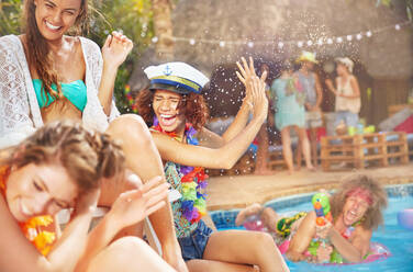 Young man with squirt gun spraying women friends at summer swimming pool - CAIF27235