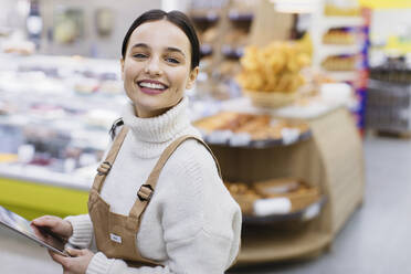 Portrait happy, confident female grocer with digital tablet working in supermarket - CAIF27276