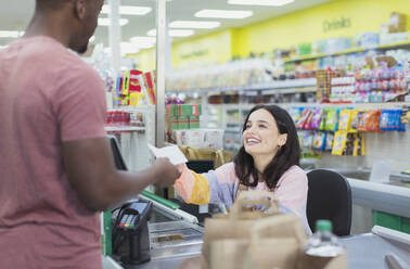 Lächelnde Kassiererin gibt dem Kunden an der Supermarktkasse eine Quittung - CAIF27278