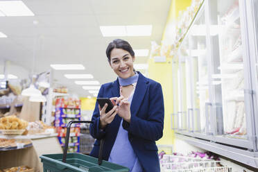 Portrait lächelnde, selbstbewusste Frau mit Smartphone beim Einkaufen im Supermarkt - CAIF27281