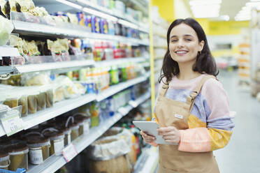 Portrait confident, smiling female grocer with digital tablet in supermarket - CAIF27284