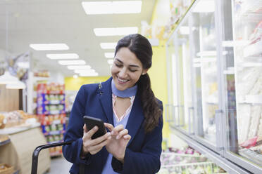 Lächelnde Frau mit Smartphone beim Einkaufen im Supermarkt - CAIF27288