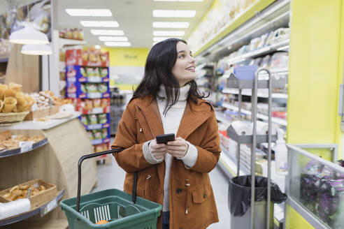 Frau mit Smartphone beim Einkaufen im Supermarkt - CAIF27289
