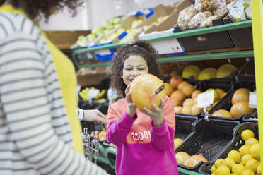 Smiling daughter showing grapefruit to mother in supermarket - CAIF27290